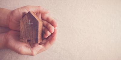 hands holding a small wooden church with a cross on it